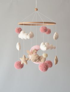 a pink and white baby mobile hanging from a wooden frame with clouds, stars and a bunny on it