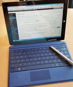 an open laptop computer sitting on top of a wooden table next to a blue keyboard