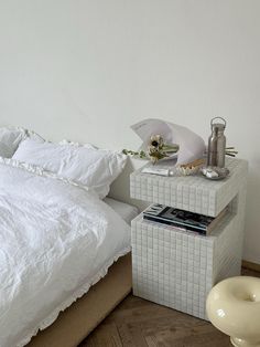 a white bed sitting next to a night stand on top of a wooden floor