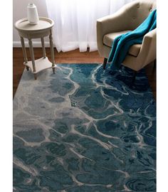 a blue rug with waves on it in front of a white chair and table next to a window