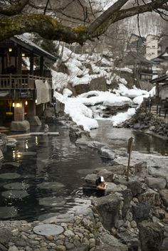 a river running through a snow covered forest next to a small building with a clock on it