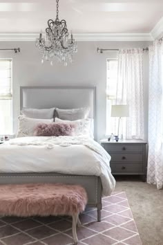 a bedroom with a chandelier hanging from the ceiling and a bed in front of two windows