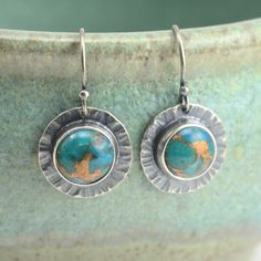 "These all sterling silver earrings feature 8mm blue mohave turquoise cabochons, bezel set against hammered round backplates.  The earrings have been oxidized to highlight the texture. They measure about 1 inch long, including the earwire, and about 1/2 inch wide. To give a sense of the size, a sample was photographed in my hand. You have a choice of earwire styles. Please see the last picture for a comparison of the two style options. Earring measurements listed above are for the ball end earwires (A.); the lever back earwires add about 1/8\" in length.  A. Ball end earwires (shown in earring pictures) (sterling silver,.68mm thick) B. Leverback earwires (sterling silver,.78mm thick) The earrings pictured are the exact ones you will receive  Please read my shipping and policies page on the Hammered Turquoise Sterling Silver Jewelry, Turquoise Hammered Sterling Silver Jewelry, Turquoise Soldered Sterling Silver Earrings, Sterling Silver Patina Earrings, Silversmith Jewellery, Turquoise Earrings, Bezel Setting, Designer Earrings, Sterling Silver Earrings