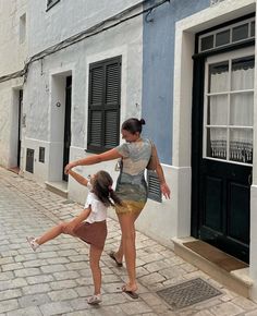 two girls are playing with each other on the sidewalk in front of some buildings and doors