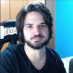 a man with long hair and beard sitting in front of a desk