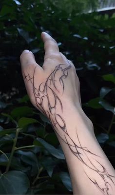 a person's hand with a tattoo on it in front of some bushes and trees