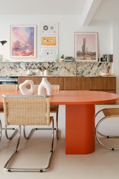 an orange table and chairs in a room with pictures on the wall behind it,