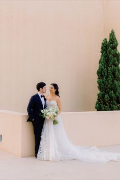 a bride and groom standing next to each other in front of a building with trees