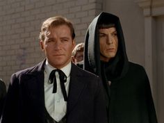 a man in a suit and tie standing next to another man wearing a hoodie