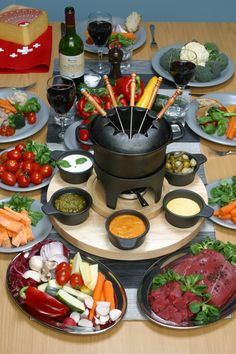 a table topped with lots of plates and bowls filled with different types of food next to wine glasses