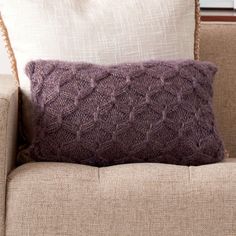 a purple knitted pillow sitting on top of a couch next to a white pillow