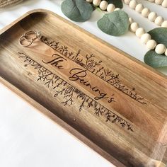 a wooden tray with wedding rings on it next to beads and greenery in the background