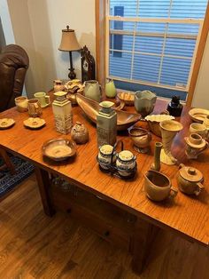 a wooden table topped with lots of bowls and plates on top of it next to a window