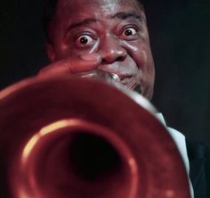 a man holding a red trumpet in his right hand and looking up at the camera