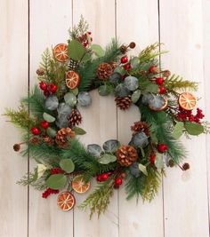 a christmas wreath with oranges, pine cones and greenery on a white wooden background