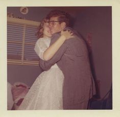 a man and woman embracing each other in a room with blinds on the window sill