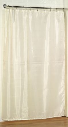 a white shower curtain hanging on the side of a bath tub in a bathroom with wooden floors