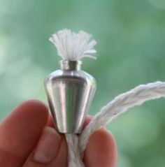 a hand holding a tiny silver object with white yarn