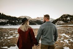 a man and woman holding hands while standing in the middle of a field with snow on the ground