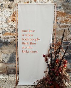 a white banner with words on it next to a potted plant in front of a stone wall