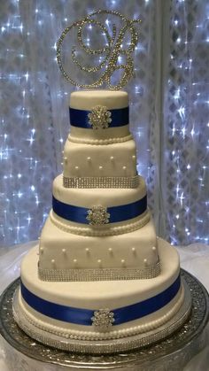 a three tiered wedding cake with blue and white ribbon on the bottom is topped with a monogram