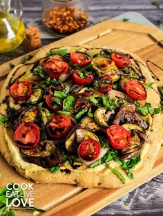 a pizza with tomatoes, mushrooms and spinach on a cutting board next to olives