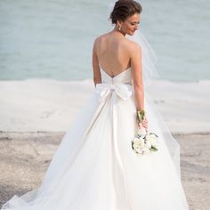 a woman in a wedding dress is standing on the beach with her back to the camera