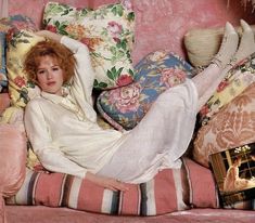 a woman laying on top of a pink couch covered in pillows