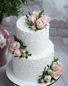 a three tiered white wedding cake with pink flowers on top and greenery around it