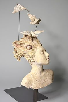 a sculpture of a woman's head with birds flying around her and one bird on top of the head