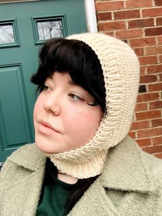 a young woman wearing a knitted hat and coat in front of a green door