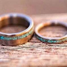 two wedding rings with turquoise and gold inlays sitting on a piece of wood