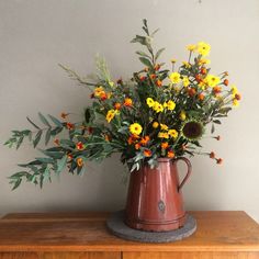 a vase filled with yellow and orange flowers on top of a wooden table next to a wall