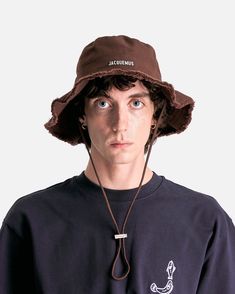 Jacquemus Le Bob Artichaut in Brown. This bucket hat features a frayed brim, silver metal logo at the front, topstitched brim and a long adjustable strap at the back. Metal Logo, Metallic Logo, The Back, Metallic Silver, Bucket Hat, Adjustable Straps, Hats, Silver