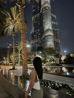 a woman standing next to a palm tree in front of a tall building at night