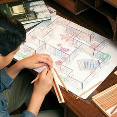 a young boy sitting at a desk drawing on paper with pencils in front of him