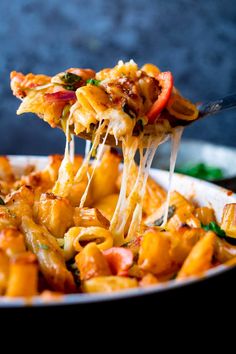 a fork full of pasta being lifted from a skillet with cheese and vegetables on it