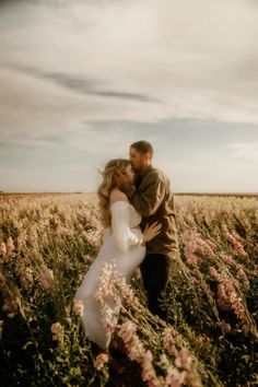 a bride and groom kissing in a field of wildflowers under a cloudy sky