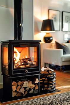 Modern black log burner in a living room with built-in log storage and contemporary decor. Wood Stove Baby Proofing, Modern Wood Burner Fireplace, Large Wood Stove, Wood Stove With Wood Storage, Log Burner Hearth Ideas, Wood Burner Living Room, Witches Hearth, Corner Wood Stove Ideas, Wood Stoves Ideas Living Rooms