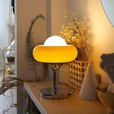 a table lamp sitting on top of a wooden counter next to a vase and plant