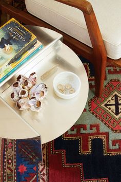 a coffee table with books and bowls on it in front of a white chair next to a rug