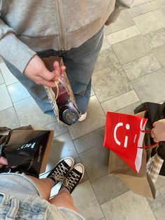 two people standing on the floor with bags and sodas in their hands, one holding a red shopping bag