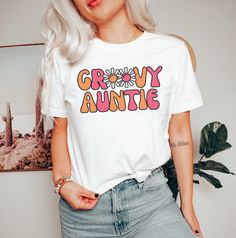 a woman with blonde hair wearing a white t - shirt that says groovy auntie