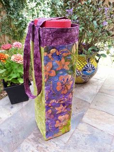 a purple and green tote bag sitting on top of a stone floor next to potted plants