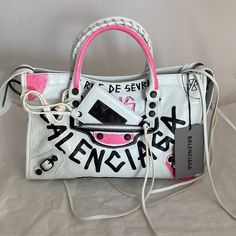 Authentic Balenciaga Limited Edition City S Graffiti Handbag In White With Black And Pink Logo Graffiti. Larger Than The Mini In A Desirable Size Small. Very Roomy And Beautifully Done In A Soft, Supple Leather. Rolled Whip Stitched Double Handles, Front Center Outer Pocket With Attached Framed Mirror. All Dark Bronze Hardware. Detachable And Adjustable Shoulder Strap. Tasseled Zips. Double Inner Slip Pocket And One Zip Pocket. Black Canvas Lining. Eye Catching And Show Stopping In These Bold Co Designer White Top Handle Shoulder Bag, Designer White Shoulder Bag For Spring, Designer White Bag With Dust Bag, Luxury White Shoulder Bag For Spring, Designer Shoulder Bag For Spring, White Designer Bags With Branded Hardware, Balenciaga Small City, Balenciaga Giant City Bag, Balenciaga Mini Bag