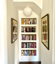 there is a bookshelf with many books on it in the hallway next to two framed pictures