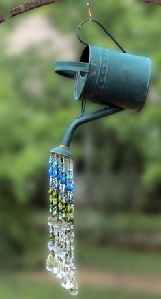 a blue bird feeder hanging from a tree branch with beads and chains attached to it