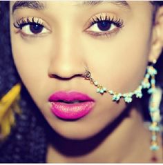 a woman with long braids and pink lipstick is wearing a nose chain that has beads on it