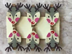 three wooden reindeer magnets with pink noses and antlers on them, mounted to a wall