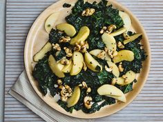 a wooden plate topped with spinach and apples on top of a table next to utensils